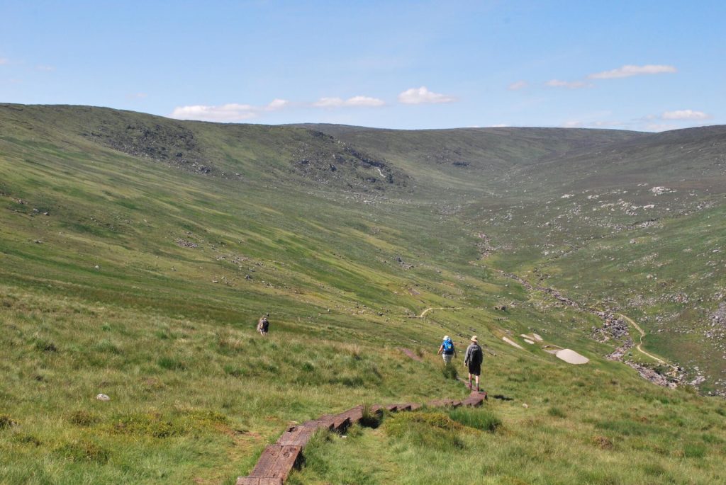 Two hikers walking away from the camera amidst the green vast landscape of Wicklow Mountains National Park in Ireland on a tour with Footfalls Walking Holidays