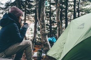 A person holding a cup next to a tent, enjoying nature